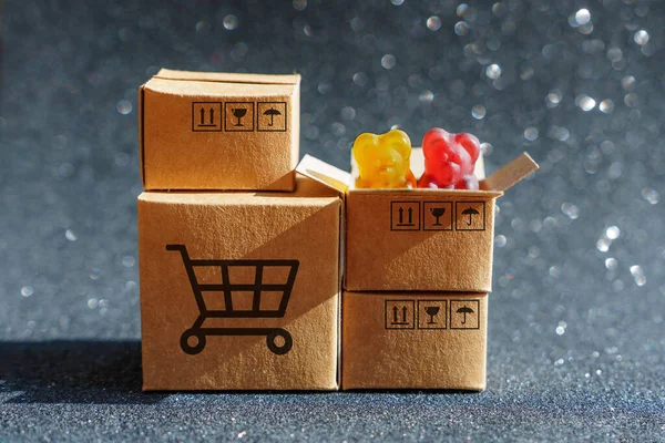 Miniature cardboard boxes with shipping labels isolated on black sparkling background. Two colorful gummy bears peeping out of a box.