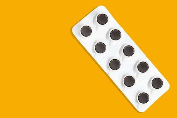 Pharmaceutical blister package with tiny coffee cups isolated on yellow background. Coffee as a cure concept.