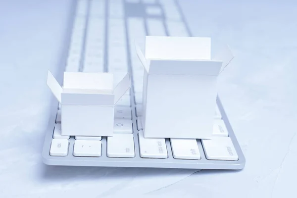 Small white shipping boxes placed on a keyboard. E-commerce delivery and supply concept.