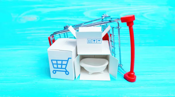 Small labeled shipping boxes with tiny bathtub placed in an overturned toy push trolley isolated on a blue wooden background. Creative bathroom supplies concept.