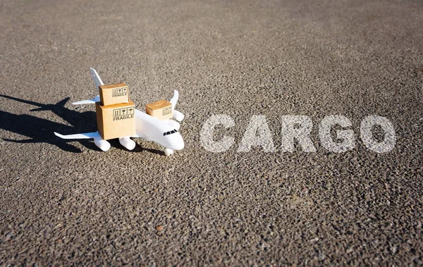 Word Cargo小さな出荷ボックスがロードされたおもちゃの飛行機の前の滑走路に書かれた — ストック写真