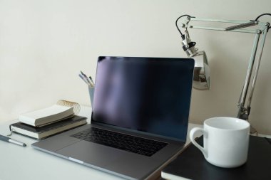 Siyah ekranlı modern stil kişisel laptop. Serbest sanatçı ya da tasarımcı işyeri. Temiz görüntü. Masa lambası. Boya fırçaları. Çizim ve yazım için not defterleri. Beyaz bardak. Elektronik aletler.