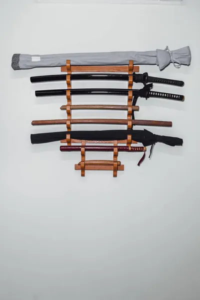 Speciální stojan na bílé stěně pro trénink mečů z dubového dřeva a železa. Tradiční japonské cvičné zbraně pro různé disciplíny bojových umění. — Stock fotografie