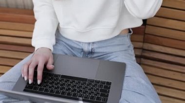 Bahçede dizüstü bilgisayar kullanan genç bir kadın. Müşteriyle internet üzerinden iletişim kuruyor. Rahat bir iş yeri, uzaktan çalışma, E öğrenme konsepti. E- posta denetleniyor, sosyal ağda mesaj yazılıyor.