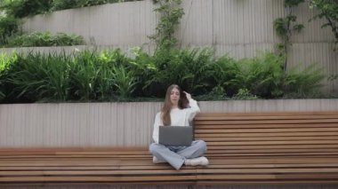 Bahçede dizüstü bilgisayar kullanan genç bir kadın. Müşteriyle internet üzerinden iletişim kuruyor. Rahat bir iş yeri, uzaktan çalışma, E öğrenme konsepti. E- posta denetleniyor, sosyal ağda mesaj yazılıyor.