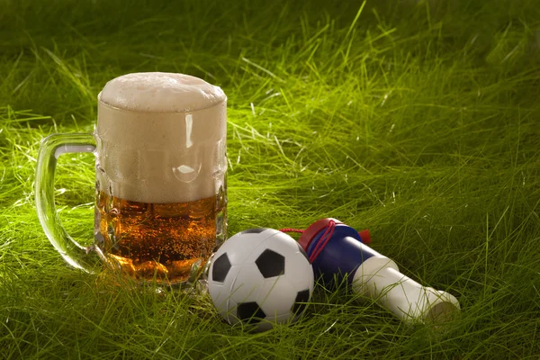 Caneca de cerveja fresca lager, vuvuzela e pequena bola de futebol sobre o g — Fotografia de Stock