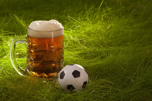 Becher frisches Lagerbier und kleiner Fußball auf dem Rasen. — Stockfoto