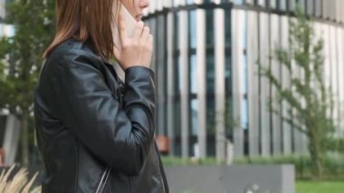 İş merkezinin yakınında bir müşteriyle akıllı telefondan konuşan gülümseyen bir iş kadını.