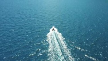 Mavi denizde yüzen beyaz bir teknenin drone görüntüsü. Yüksek hızda hareket eden beyaz bir yat.. 