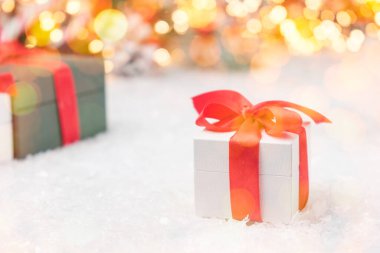 Karda kırmızı kurdele ve arka planda ışıklar olan Noel hediyesi kutuları..