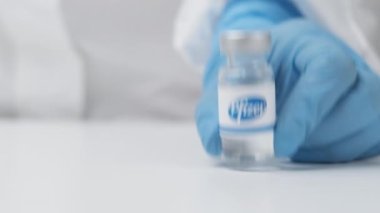 Sağlık çalışanı tarafından masaya konan plastik eldiven ve PPE takım elbiseli Pfizer şişesi, Mayıs 2021, San Francisco, ABD