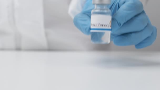 Флакон AstraZeneca с лекарствами, поставленными на стол медицинским работником в резиновых перчатках и костюме СИЗ, май 2021 года, Сан-Франциско, США — стоковое видео