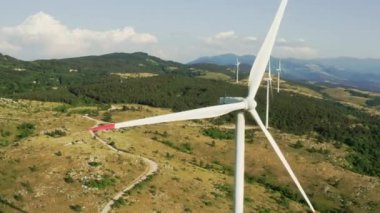 Kamera dağlarda dönen bir rüzgar türbininin etrafında dönüyor. Yazın bir rüzgar çiftliğinin havadan görünüşü. Yeşil ve yenilenebilir elektrik üretimi.