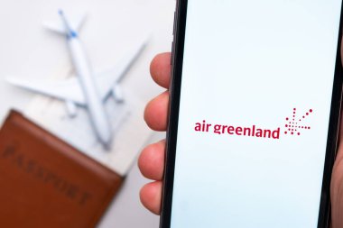 Akıllı telefon ekranındaki Air Greenland Havayolları uygulaması. Beyaz oyuncak bir uçak ve pasaport, hafif bir yüzeyi olan bir masada yatıyor. Kasım 2021, San Francisco, ABD.