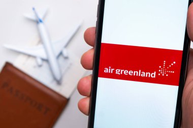 Akıllı telefon ekranındaki Air Greenland Havayolları uygulaması. Beyaz oyuncak bir uçak ve pasaport, hafif bir yüzeyi olan bir masada yatıyor. Kasım 2021, San Francisco, ABD.