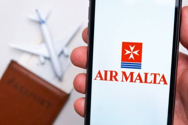 Airmalta Havayolları uygulaması akıllı telefon ekranının elinde. Beyaz oyuncak bir uçak ve pasaport, hafif bir yüzeyi olan bir masada yatıyor. Kasım 2021, San Francisco, ABD.