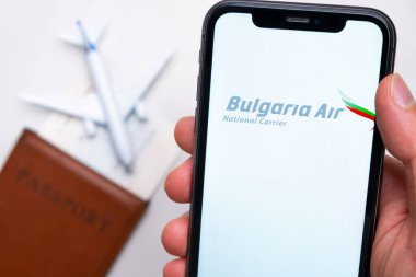 Bulgaristan Hava Yolları uygulaması cep telefonu ekranında arka planda uçak, biniş kartı ve pasaportla el ele geziyor. Havayolları mobil uygulaması kavramı. Kasım 2021, San Francisco