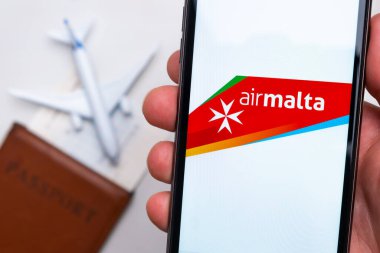 Airmalta Havayolları uygulaması akıllı telefon ekranının elinde. Beyaz oyuncak bir uçak ve pasaport, hafif bir yüzeyi olan bir masada yatıyor. Kasım 2021, San Francisco, ABD.
