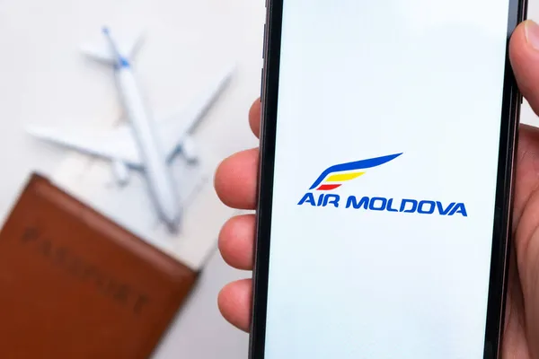 Aplicación Air Moldova Airline en la pantalla del teléfono inteligente mans mano. Un avión de juguete blanco y un pasaporte están acostados en una mesa con una superficie liviana.Noviembre 2021, San Francisco, Estados Unidos. — Foto de Stock