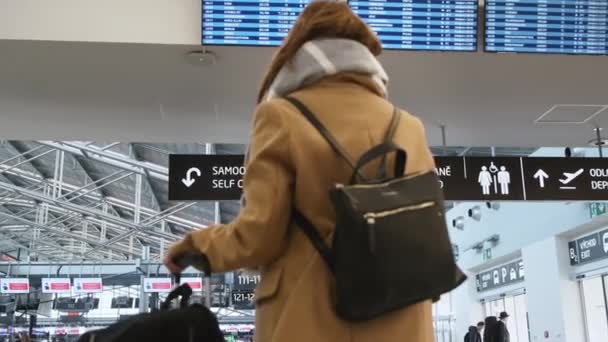 Sırtında siyah çantasıyla, tabelaların önünde dikilmiş, Çek Cumhuriyeti 'nin Prag havaalanına varış ve kalkış panosuna bakan biraz bulanık bir bayan yolcu. Düşük sezon seyahat konsepti. — Stok video
