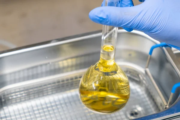 Scientist in blue rubber puts a yellow solution in the flask for dissolving or extraction into ultrasound bath. Urea analysis. Clinical, toxicological and forensic analysis — Stock Photo, Image