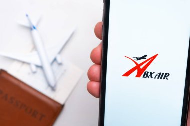 Abx Air Havayolları uygulaması erkek eliyle akıllı telefon ekranında. Oyuncak uçak, pasaport ve biletler masada. Kasım 2021, San Francisco, ABD.