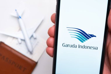 Garuda Endonezya Havayolları uygulaması erkek eliyle cep telefonu ekranında. Pasaport, levrek arka planda beyaz bir uçağın yanında. Kasım 2021, San Francisco, ABD.