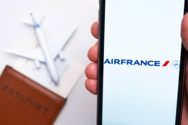 Airfrance Havayolları uygulaması erkek eliyle akıllı telefon ekranında. Oyuncak uçak, pasaport ve biletler masada. Kasım 2021, San Francisco, ABD.
