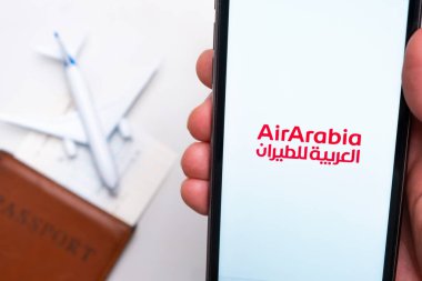 AirArabia Havayolları uygulaması Man 's Hand' deki akıllı telefon ekranında. Oyuncak uçak, pasaport ve biletler masada. Kasım 2021, San Francisco, ABD.