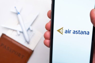 Air Asterana Havayolları uygulaması Man 's Hand' de akıllı telefon ekranında. Oyuncak uçak, pasaport ve biletler masada. Kasım 2021, San Francisco, ABD.