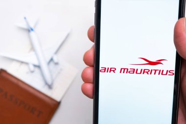 Air Mauritius Havayolları uygulaması erkek eliyle akıllı telefon ekranında. Oyuncak uçak, pasaport ve biletler masada. Kasım 2021, San Francisco, ABD.