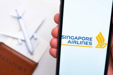 Singapur Havayolları uygulaması erkeklerin elinde cep telefonu ekranında. Pasaport, levrek arka planda beyaz bir uçağın yanında. Kasım 2021, San Francisco, ABD.