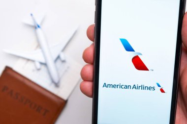 American Airlines uygulaması akıllı telefon ekranında gösteriliyor. Arka planda bulanık bir uçak, pasaport ve biniş kartı var. Kasım 2021, San Francisco, ABD.