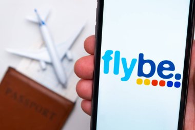 Flybe Havayolları. Bir cep telefonu ve uçuş havayolları başvurusu. Beyaz bir masada bir pasaport ve bir uçak var. Kasım 2021, San Francisco, ABD.