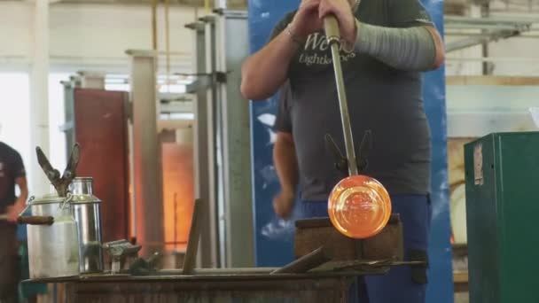 Glastillverkaren blåser ut och bildar varm glaskula vid arbetsbänken — Stockvideo