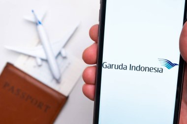 Garuda Endonezya Havayolları uygulaması akıllı telefon ekranında gösteriliyor. Arka planda bulanık bir uçak, pasaport ve biniş kartı var. Kasım 2021, San Francisco, ABD.