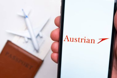 Cep telefonu ekranında Avusturya Havayolları uygulama logosu. Arka planda bulanık bir uçak görüntüsü, pasaport ve biniş kartı. Kasım 2021, San Francisco, ABD.