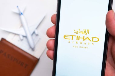 Etihad Havayolları uygulaması akıllı telefon ekranında gösteriliyor. Arka planda bulanık bir uçak, pasaport ve biniş kartı var. Kasım 2021, San Francisco, ABD.