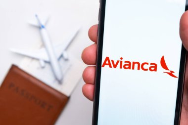 Avianca Havayolları uygulama logosu cep telefonu ekranında. Arka planda bulanık bir uçak görüntüsü, pasaport ve biniş kartı. Kasım 2021, San Francisco, ABD.