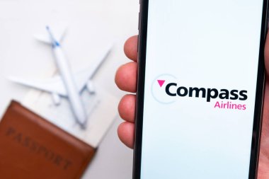 Pusula Havayolları uygulama logosu cep telefonu ekranında. Arka planda bulanık bir uçak görüntüsü, pasaport ve biniş kartı. Kasım 2021, San Francisco, ABD.