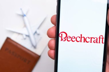 Beechcraft Airlines app logo on the screen of mobile phone. A blurry image of a plane, a passport and boarding pass on the background. November 2021, San Francisco, USA. clipart