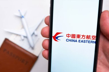China Eastern Havayolları uygulama logosu cep telefonu ekranında. Arka planda bulanık bir uçak görüntüsü, pasaport ve biniş kartı. Kasım 2021, San Francisco, ABD.