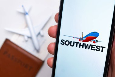 Güneybatı Havayolları uygulaması cep telefonu ekranında arka planda uçak, uçuş kartı ve pasaportlu adamlar var. Havayolları mobil uygulaması kavramı. Kasım 2021, San Francisco, ABD