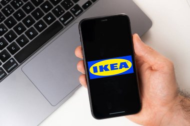 Akıllı telefon ekranında Ikea mobil uygulaması. Açık bir dizüstü bilgisayarın yanında bir adamın elinde cep telefonu. Kasım 2021, San Francisco, ABD