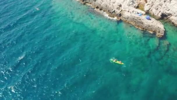 As pessoas remar caiaque colorido ao longo do mar passado praia rochosa — Vídeo de Stock