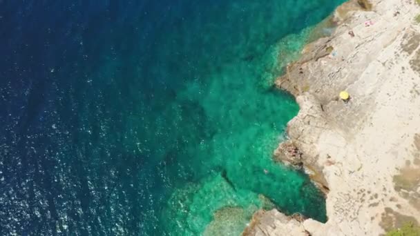 Οι τουρίστες ξεκουράζονται σε βραχώδη παραλία κοντά σε γαλήνιο γαλάζιο κόλπο της θάλασσας — Αρχείο Βίντεο