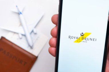 Royal Brunei Havayolları logosu cep telefonu ekranında, arka planda uçak, pasaport ve uçuş kartı var. Havayolları mobil uygulaması kavramı. Kasım 2021, San Francisco, ABD.