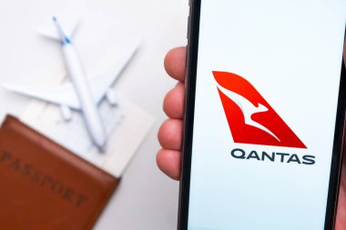 Arka planda uçak, pasaport ve uçuş kartı olan cep telefonu ekranında Qantas Havayolları logosu var. Havayolları mobil uygulaması kavramı. Kasım 2021, San Francisco, ABD.