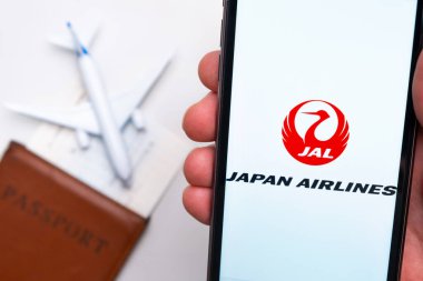 Japon Hava Yolları Havayolları uygulaması akıllı telefon ekranında gösteriliyor. Arka planda bulanık bir uçak, pasaport ve biniş kartı var. Kasım 2021, San Francisco, ABD.