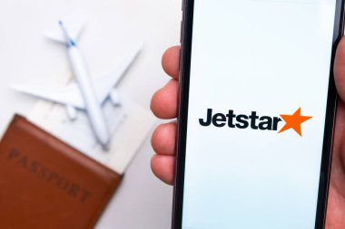 Jetstar Havayolları uygulaması akıllı telefon ekranında gösteriliyor. Arka planda bulanık bir uçak, pasaport ve biniş kartı var. Kasım 2021, San Francisco, ABD.